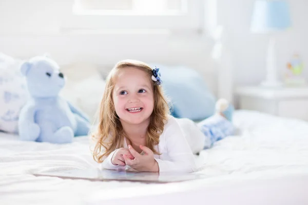 Liten flicka leker med leksak och läsa en bok i sängen — Stockfoto
