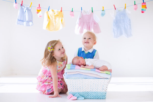 Брат и сестра целуют новорожденного ребенка
