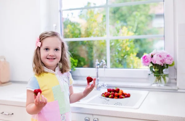 Маленькая девочка стирает клубнику на белой кухне — стоковое фото