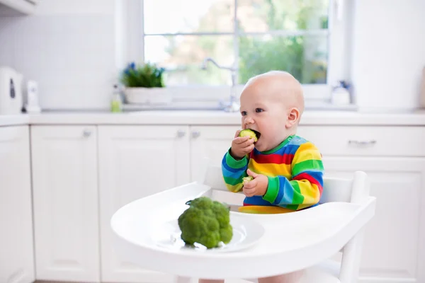 Маленький хлопчик їсть брокколі на білій кухні — стокове фото