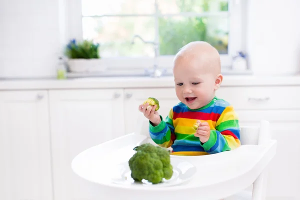 Menino comendo brócolis na cozinha branca — Fotografia de Stock