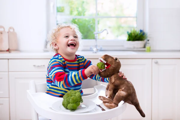 Kleiner Junge füttert Spielzeug-Dinosaurier mit Brokkoli — Stockfoto