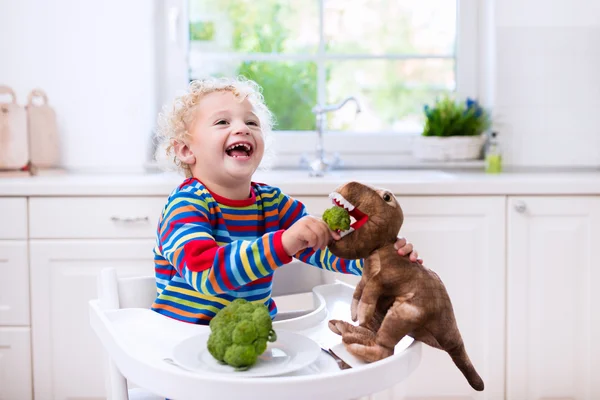 Bambino che nutre broccoli al dinosauro giocattolo — Foto Stock