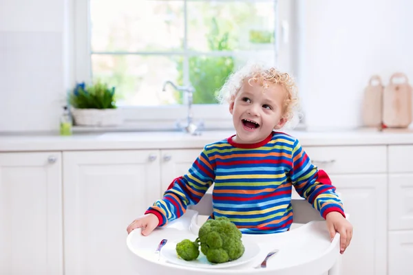 Niño comiendo brócoli en cocina blanca — Foto de Stock