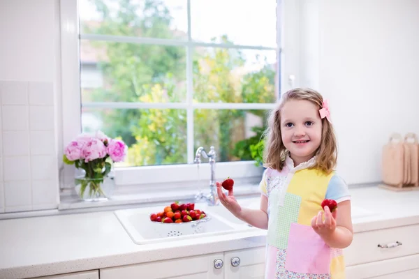 Little girl washing strawberries in white kitchen