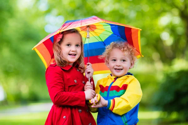 Kinder spielen im Regen unter buntem Regenschirm — Stockfoto