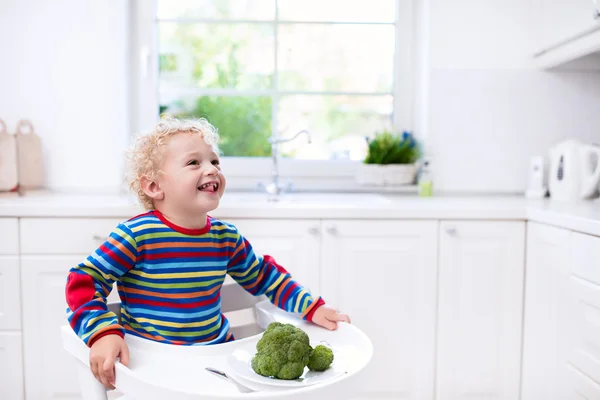 Menino comendo brócolis na cozinha branca — Fotografia de Stock