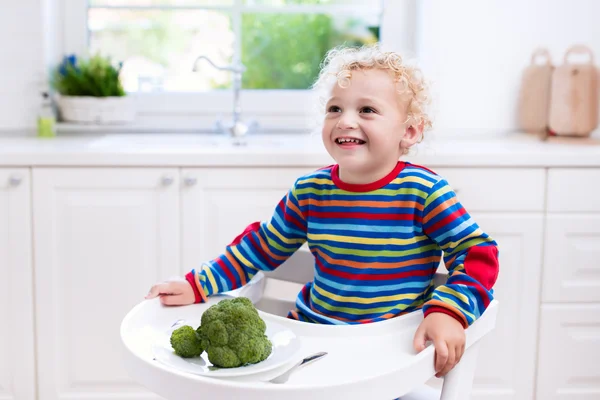 Malý chlapec jíst brokolici v bílé kuchyni — Stock fotografie