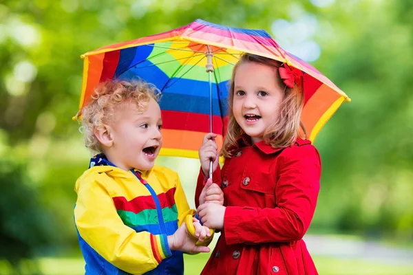 Niños jugando bajo la lluvia bajo un colorido paraguas —  Fotos de Stock