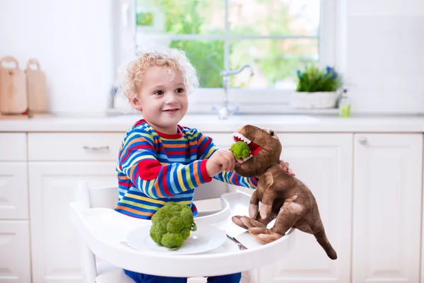 Kleiner Junge füttert Spielzeug-Dinosaurier mit Brokkoli — Stockfoto