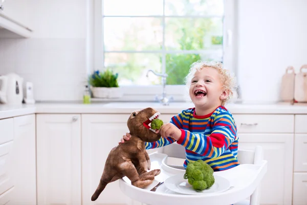 Мальчик кормит брокколи игрушечного динозавра — стоковое фото