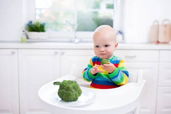 Little boy eating broccoli in white kitchen — Stock Photo, Image