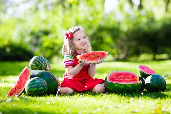 Liten flicka äter vattenmelon i trädgården — Stockfoto