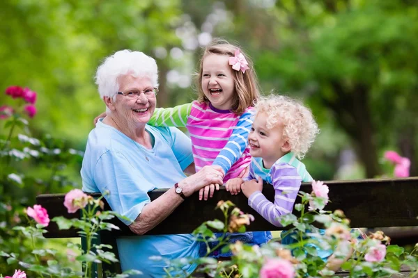 Grandmother and kids sitting in rose garden — Stock Photo, Image