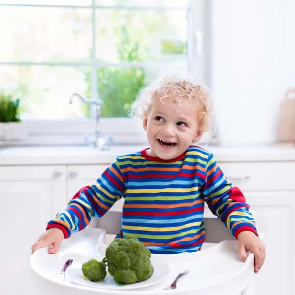 Malý chlapec jíst brokolici v bílé kuchyni — Stock fotografie