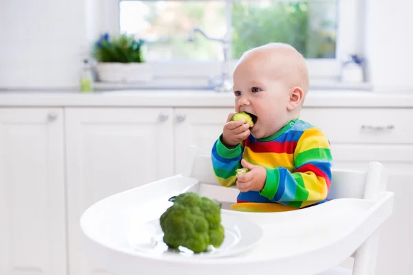 Liten gutt som spiser brokkoli på hvitt kjøkken – stockfoto