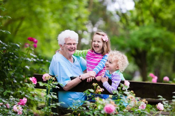 Grandmother and kids sitting in rose garden — Stock Photo, Image