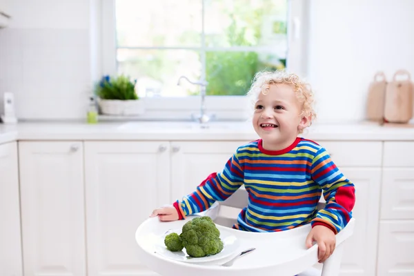 Niño comiendo brócoli en cocina blanca — Foto de Stock