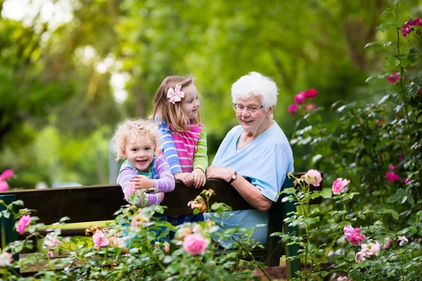 Grandmother and kids sitting in rose garden — Stock Photo, Image