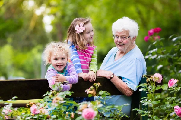 Grandmother and kids sitting in rose garden — Stock Photo, Image