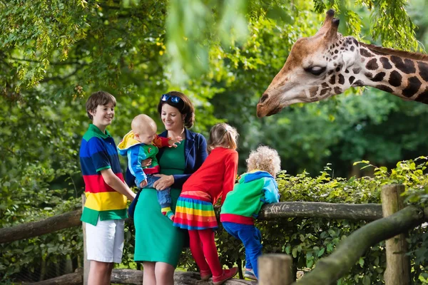 Mãe e filhos alimentando girafa no zoológico — Fotografia de Stock