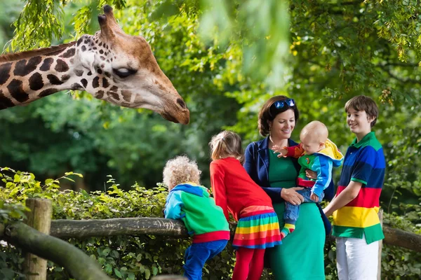 Anya és a gyerekek etetés zsiráf az állatkertben — Stock Fotó