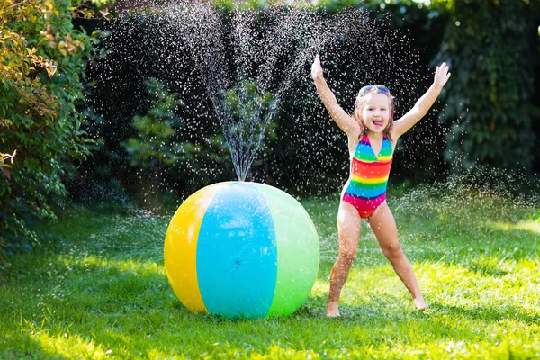 グッズ ボール、庭のスプリンクラーで遊ぶ少女 — ストック写真