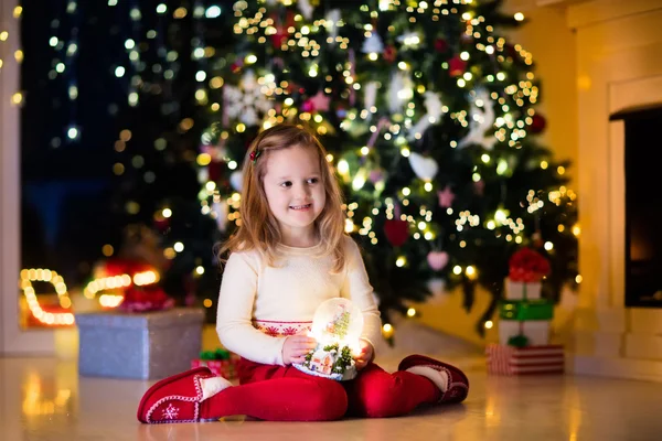 Menina segurando globo de neve sob a árvore de Natal — Fotografia de Stock