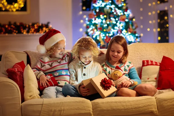 圣诞节前夕 孩子们在圣诞树和壁炉边 有孩子的家庭在家里庆祝圣诞节 穿着针织毛衣的男孩和女孩在白色沙发上打开礼物 给孩子的节日礼物 — 图库照片
