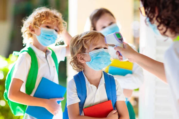 Temperature screening and medical check at school. Child in face mask in class in covid-19 outbreak. Teacher with thermometer at preschool entrance. Social distancing. Coronavirus prevention.