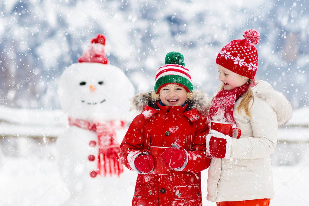 Child building snowman. Kids build snow man. Boy and girl playing outdoors on snowy winter day. Outdoor family fun on Christmas vacation in the mountains. Children play in Swiss mountain landscape.