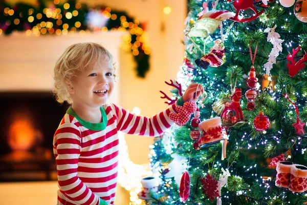 自宅でクリスマスツリーを飾る子供 クリスマスの飾りのパジャマ姿の男の子 子供たちと家族は冬の休日を祝います 子供たちはクリスマスのためにリビングルームと暖炉を飾る — ストック写真