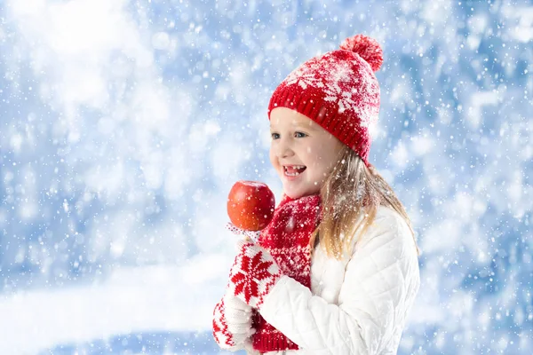 子供は冬のフェアでキャンディーアップルを食べる 子供たちは雪の中でクリスマスマーケットでトフィーリンゴを食べる 雪の日の屋外の楽しみ クリスマスシーズンの家族の休暇 子供たちは屋外で遊ぶ 子供のための冬のファッション — ストック写真