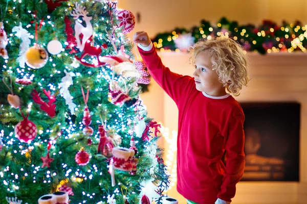 自宅でクリスマスツリーを飾る子供 クリスマスの飾りのパジャマ姿の男の子 子供たちと家族は冬の休日を祝います 子供たちはクリスマスのためにリビングルームと暖炉を飾る — ストック写真