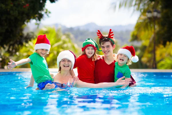 Family Christmas vacation. Kids in Santa hat jump in swimming pool. Mother and children celebrating Xmas on tropical island. Beach and water fun in winter holiday. Travel in December break.