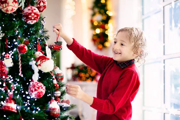 自宅でクリスマスツリーを飾る子供 クリスマスの飾りのパジャマ姿の男の子 子供たちと家族は冬の休日を祝います 子供たちはクリスマスのためにリビングルームと暖炉を飾る — ストック写真