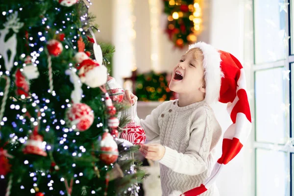 自宅でクリスマスツリーを飾る子供 クリスマスの飾りのパジャマ姿の男の子 子供たちと家族は冬の休日を祝います 子供たちはクリスマスのためにリビングルームと暖炉を飾る — ストック写真