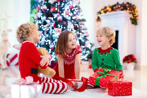 クリスマスツリーの子供たちとクリスマスの前夜の暖炉 自宅でクリスマスを祝う子供たちと家族 夏の木やオープニングプレゼントを飾るパジャマを着た男の子と女の子 子供のための休日の贈り物 — ストック写真