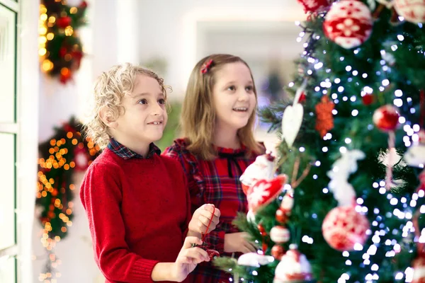 Child decorating Christmas tree at home. Little boy and girl with Xmas ornament. Family with kids celebrate winter holidays. Kids decorate living room and fireplace for Christmas.