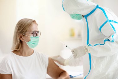 Doktor ofisinde Coronavirus aşısı aşısı. Covid-19 aşısı hastanede. Koruyucu giysili doktor hastayı muayene ediyor. Şırıngalı hemşire. Yaşlı kadın Corona virüsü kapıyor..