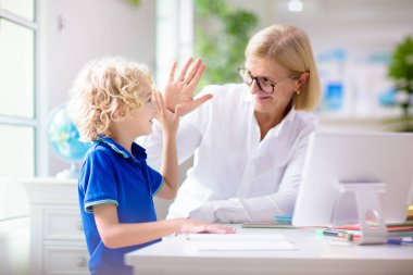 Çevrimiçi uzaktan öğrenme. Bilgisayarlı okul çocukları öğretmen ve sınıf grubuyla görüntülü konuşma yapıyorlar. Anne oğluna yardım ediyor. Çocuk evden ders çalışıyor. Koronavirüs salgınında evde eğitim.