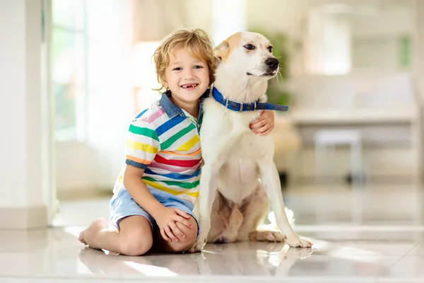 赤ちゃん犬と遊ぶ子供 子供は子犬と遊ぶ 家に小さな男の子と大きな犬 子供と友情 子供はペットと床に座っている 動物愛護 — ストック写真