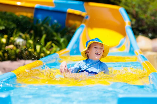 アクアパークのウォータースライダーの子供たち 熱帯のリゾートで家族の夏休みにウォータースライドで楽しんでいる子供たち 子供と赤ちゃんのためのぬれた遊び場を持つ遊園地 — ストック写真