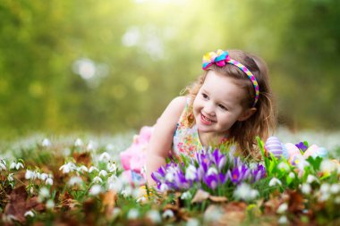 Paskalya yumurtası avına çıkan çocuk bahar çiçekleriyle çiçek açıyor. Sepetinde renkli yumurtaları olan bir çocuk. Çiçek toplayan küçük kız. Paskalya süsü, aile kutlaması, Hıristiyan gelenekleri..