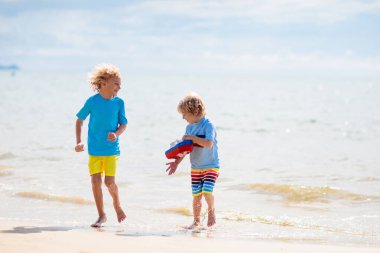Tropik plajda oynayan çocuklar. Çocuklar yaz tatilinde yüzer ve denizde oynarlar. Kum ve su eğlencesi, küçük çocuklar için güneş koruması. Okyanus kıyısında koşan ve zıplayan küçük çocuk.