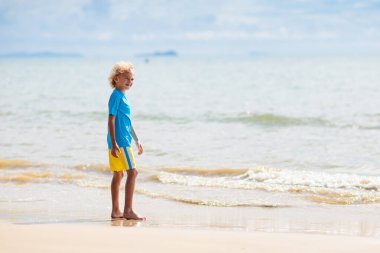 Tropik plajda oynayan çocuklar. Çocuklar yaz tatilinde yüzer ve denizde oynarlar. Kum ve su eğlencesi, küçük çocuklar için güneş koruması. Okyanus kıyısında koşan ve zıplayan küçük çocuk.