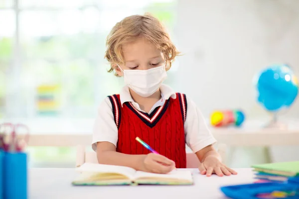 Kids in face mask in school class. Child back to school after coronavirus lockdown. Primary child in covid-19 pandemic. Safety and virus spread prevention. Student in surgical mask. Social distancing.