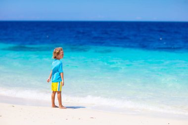 Tropik plajda oynayan çocuklar. Çocuklar yaz tatilinde yüzer ve denizde oynarlar. Kum ve su eğlencesi, güneş koruması. Okyanus kıyısında koşan ve zıplayan küçük çocuk.