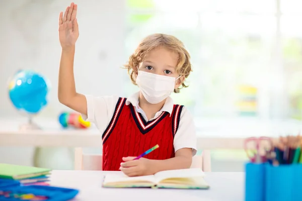 Kids in face mask in school class. Child back to school after coronavirus lockdown. Primary child in covid-19 pandemic. Safety and virus spread prevention. Student in surgical mask. Social distancing.