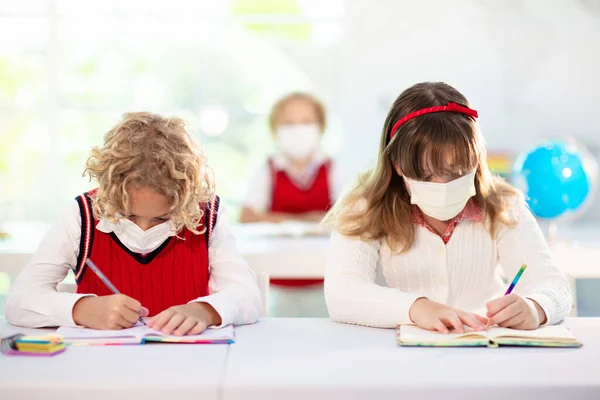 Kids in face mask in school class. Child back to school after coronavirus lockdown. Primary child in covid-19 pandemic. Safety and virus spread prevention. Student in surgical mask. Social distancing.